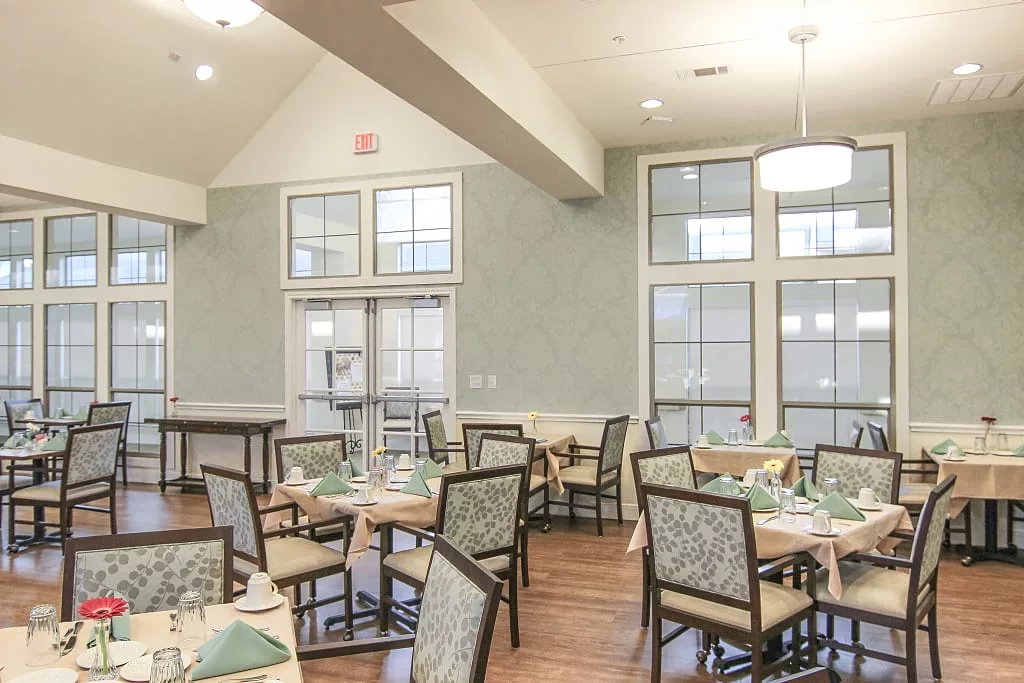 A neatly arranged dining room with several tables and chairs, featuring large windows and elegant decor.