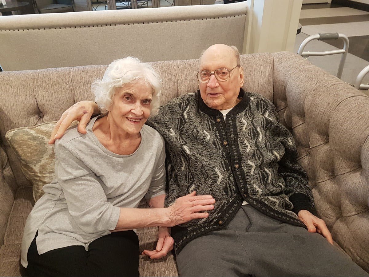 An elderly couple sitting closely together on a sofa, showing warmth and companionship.