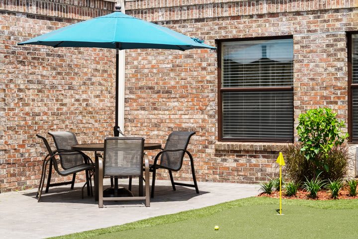 A backyard patio setup with a table, chairs, and an umbrella next to a mini putting green.