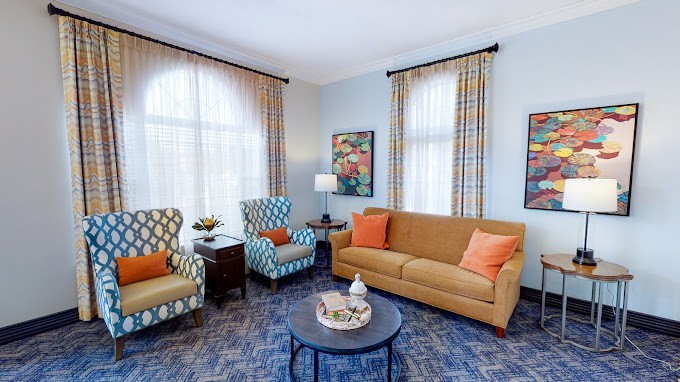 A cozy living room with a blue and orange color scheme, featuring a sofa, two patterned armchairs, a coffee table, and decorative elements.