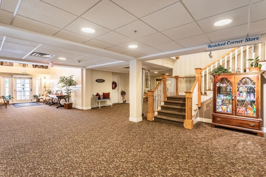 A spacious lobby area featuring carpeted floors, a staircase with wooden railings, and cozy seating.