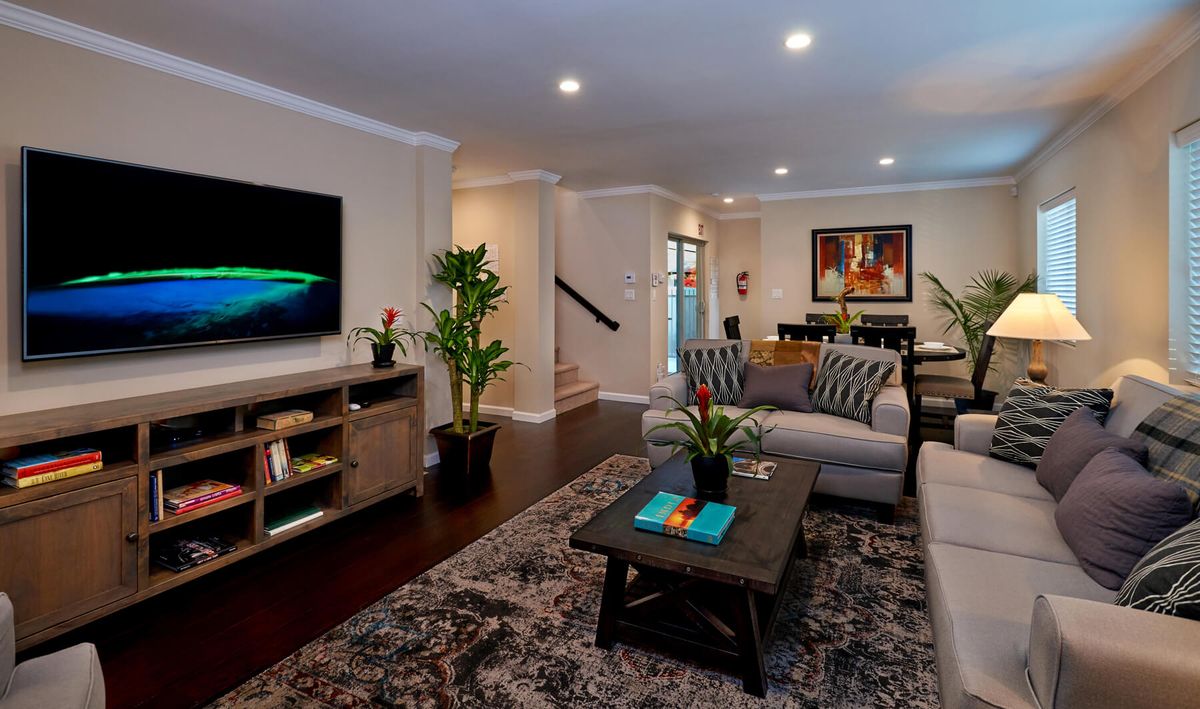 A modern living room featuring a comfortable sofa, coffee table, and large television, accented with plants and artwork.
