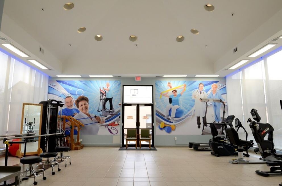 A well-lit gym interior featuring various exercise equipment and a vibrant wall mural.
