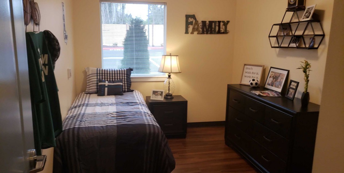 A cozy bedroom with a single bed, nightstand, and decorative 'Family' sign on the wall.