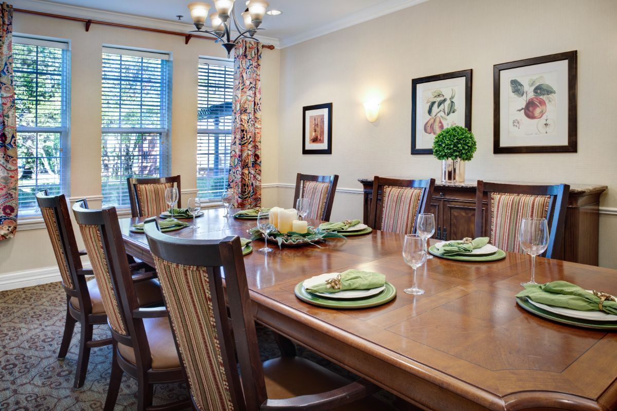 A formal dining room with a large wooden table set for dinner, surrounded by chairs and adorned with tasteful decorations.