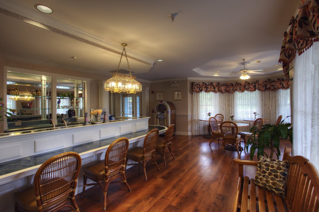 A cozy dining room with elegant chandeliers, wooden flooring, and rattan chairs.