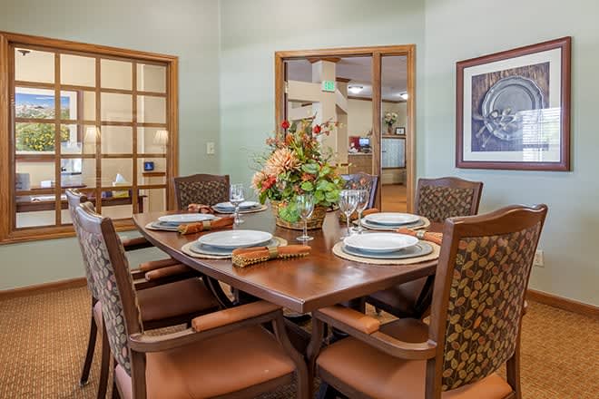 A cozy dining room featuring a wooden table, set for four, with a floral centerpiece and comfortable cushioned chairs.