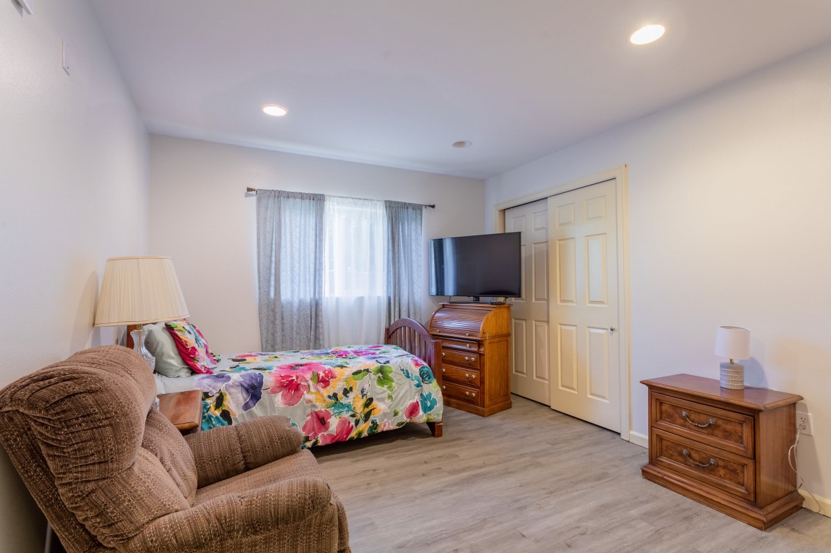 A cozy bedroom with a colorful bedspread, armchair, and wooden furniture.