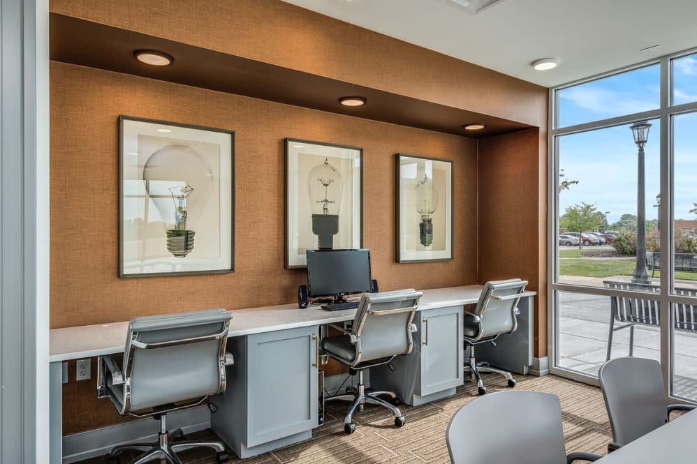 A modern office workspace featuring several desks and chairs, with a computer and framed artwork on the walls.