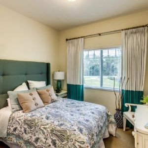 A cozy bedroom with a green headboard, floral bedding, and a window with curtains.