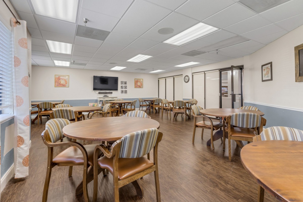 An empty cafeteria with tables and chairs arranged neatly, featuring a television on the wall.
