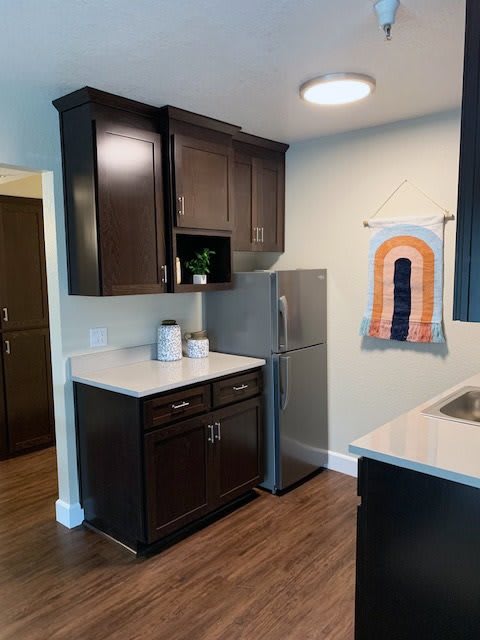 A modern kitchen space with dark cabinets, a compact refrigerator, and a decorative towel.