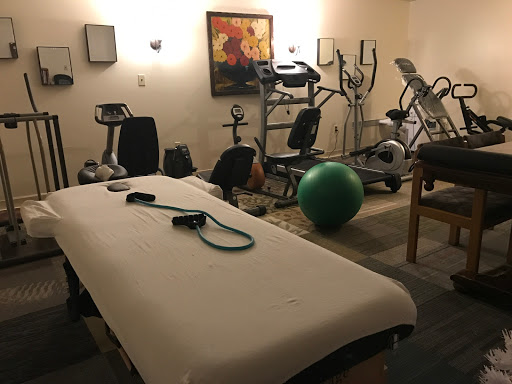A well-equipped gym area featuring various fitness machines and a treatment table.