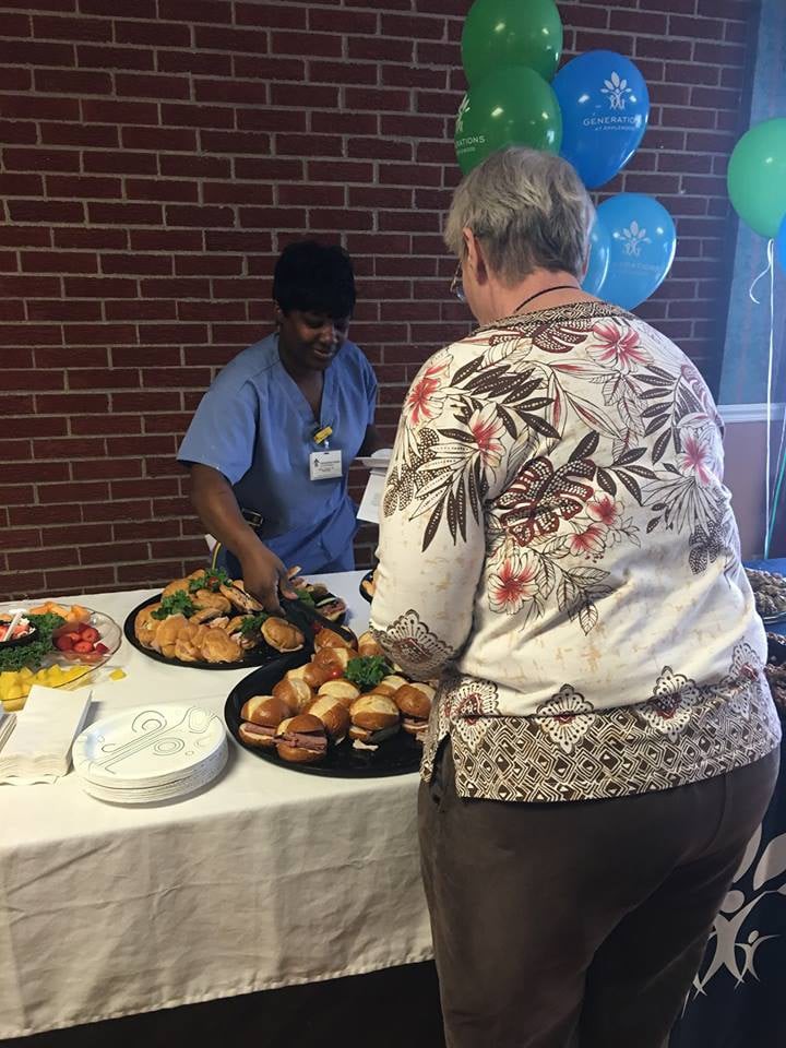 A person serving food to a guest at an indoor event with a buffet setup.
