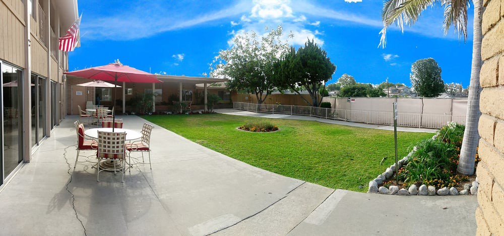 A well-maintained backyard with a green lawn, patio furniture, and trees under a clear blue sky.