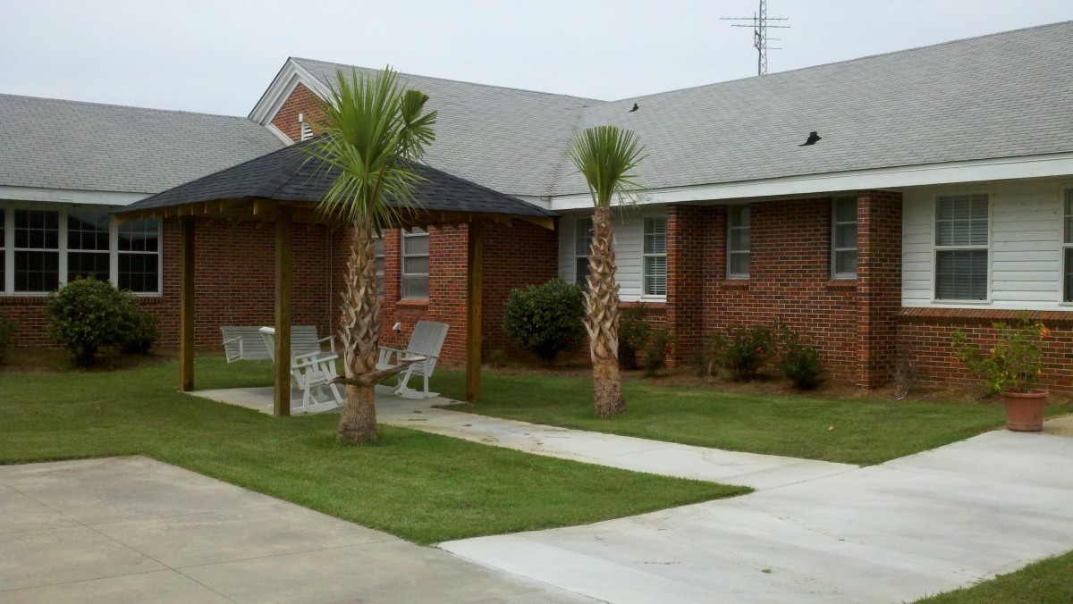 A brick house with palm trees and outdoor furniture on a neatly trimmed lawn.
