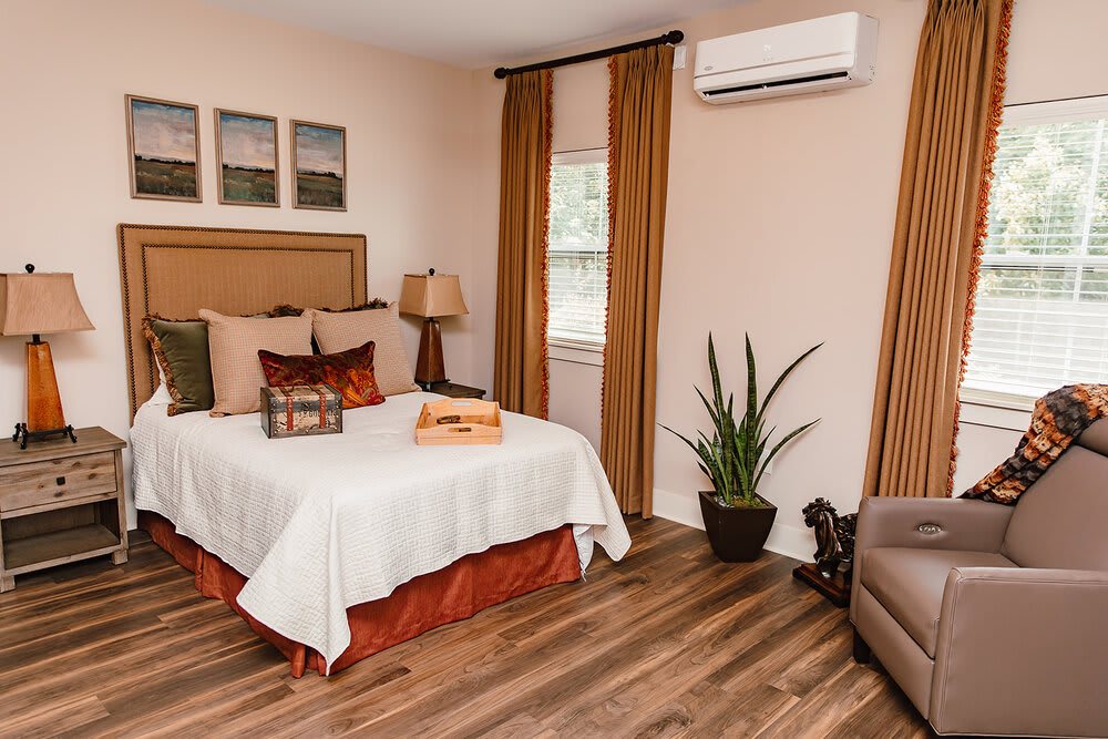 A cozy and modern bedroom featuring an air conditioner, wooden flooring, decorative pillows, and a potted plant.