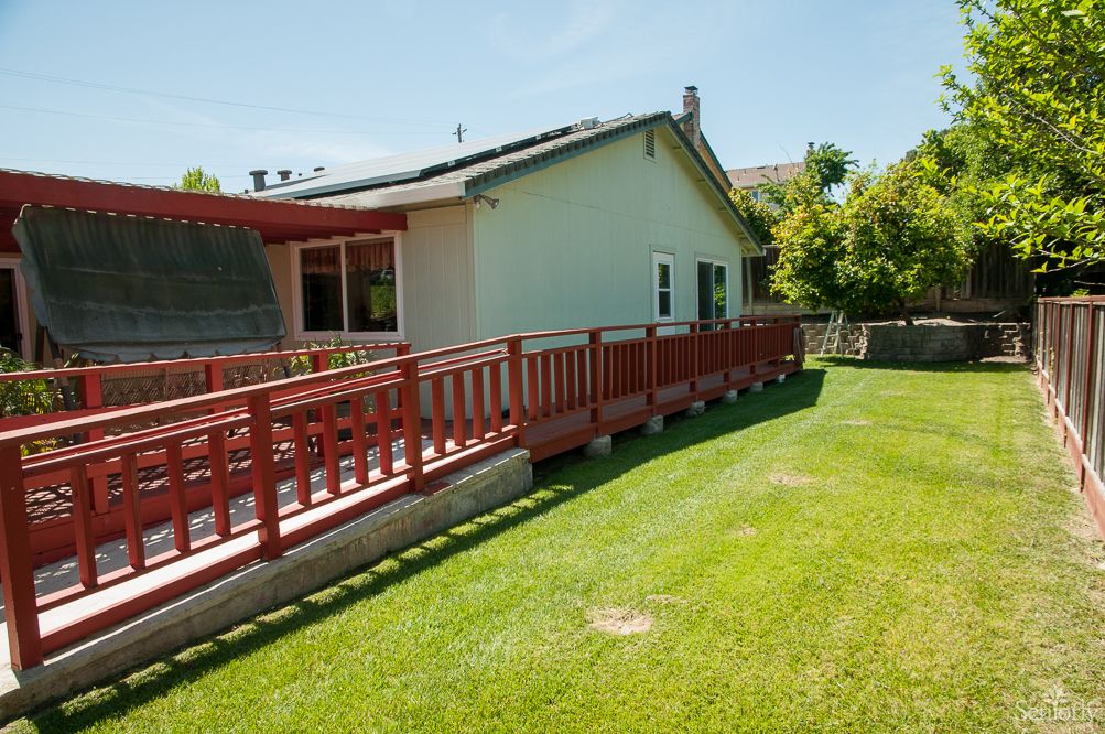 A sunny backyard view with a red wooden deck and a well-maintained lawn.