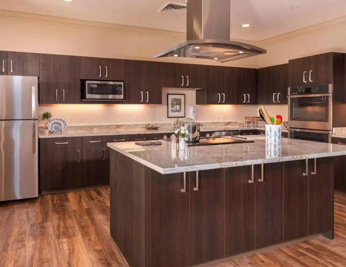 A modern kitchen featuring dark wood cabinets, a central island, and stainless steel appliances.