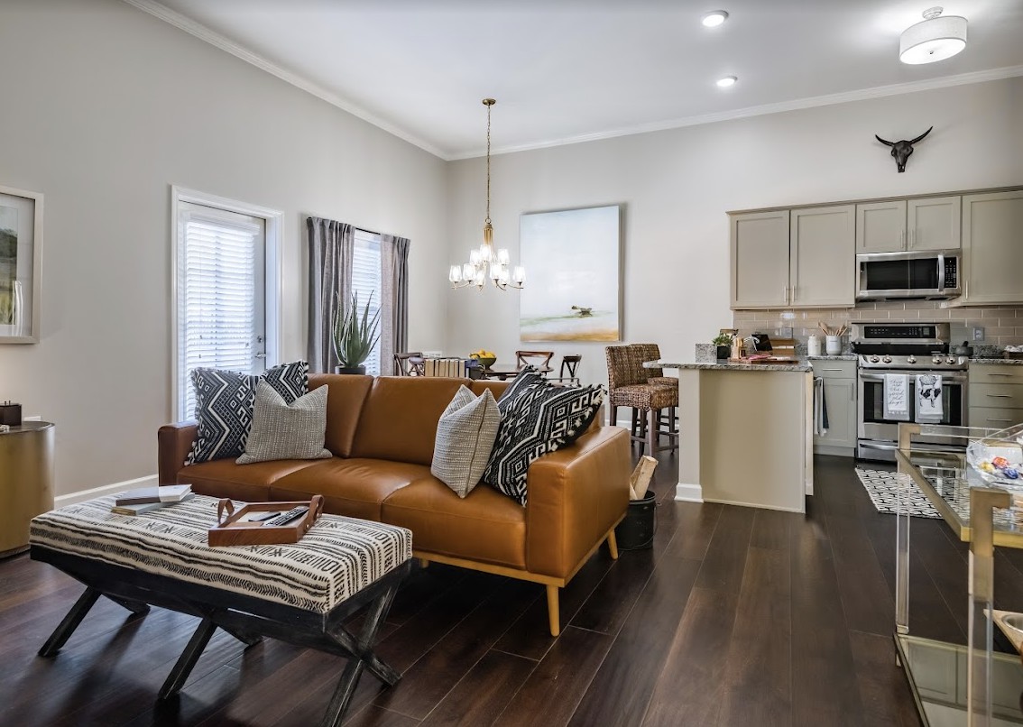 A modern, open-concept living room with a leather sofa and a view into the adjacent kitchen.
