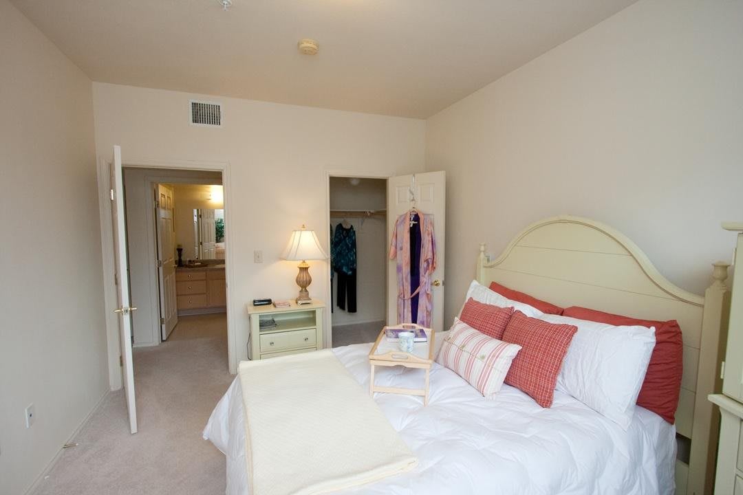 A cozy bedroom with a neatly made bed, vibrant pillows, and an open closet.
