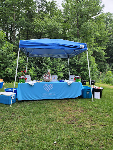 A vibrant outdoor vendor booth set up under a blue canopy, surrounded by lush greenery.