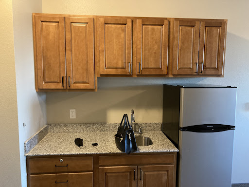 A modern kitchen featuring wooden cabinets, a granite countertop, and a compact refrigerator.