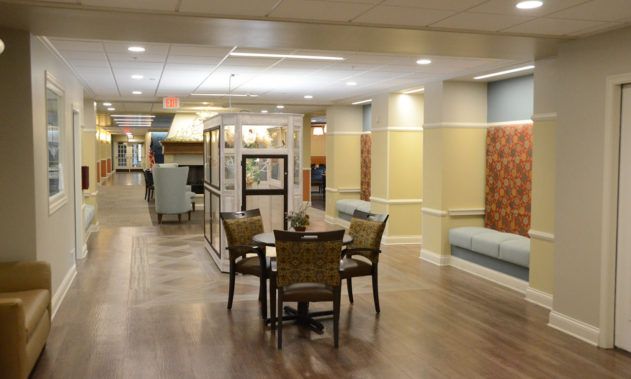 A well-lit corridor with a wooden floor, featuring a table and chairs in the center.