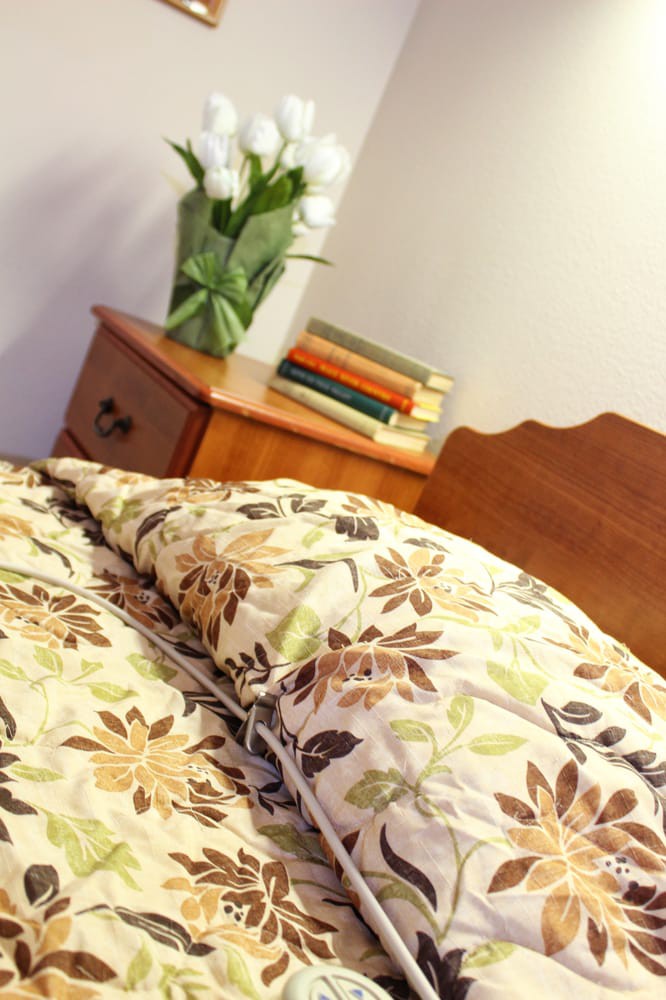 A cozy bedroom setup featuring floral bedding and a nightstand adorned with books and fresh flowers.