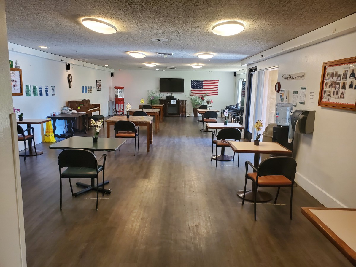 A community dining and social space with neatly arranged tables and chairs, decorated walls, and a television.