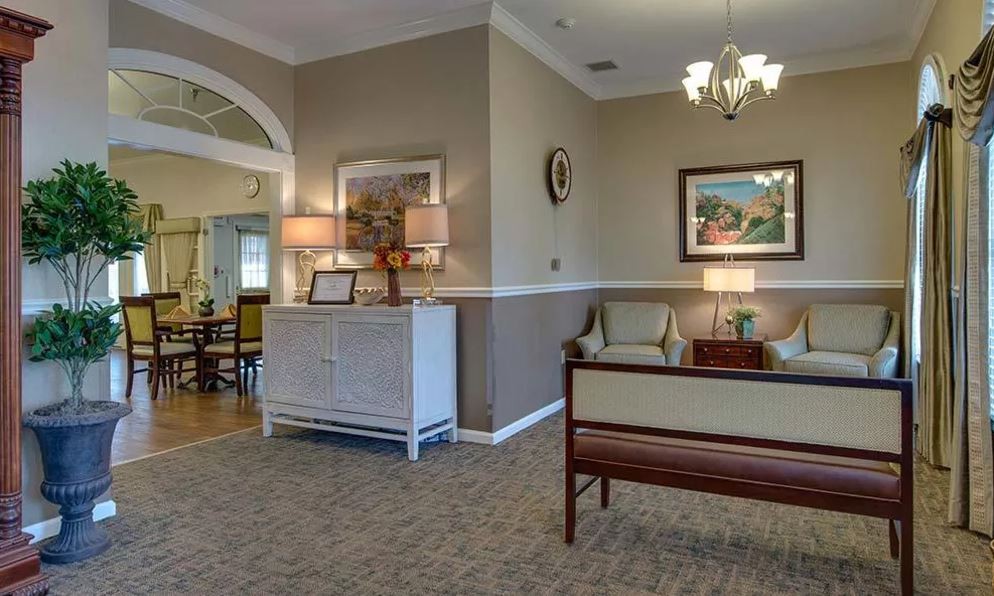 A cozy and elegantly decorated living room featuring traditional furniture, artwork on the walls, and a chandelier providing warm lighting.
