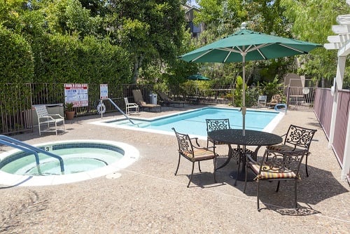 An outdoor swimming pool area with a hot tub, surrounded by patio furniture and trees.