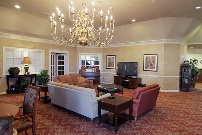 A spacious living room featuring a grand chandelier, comfortable seating, and a large television.