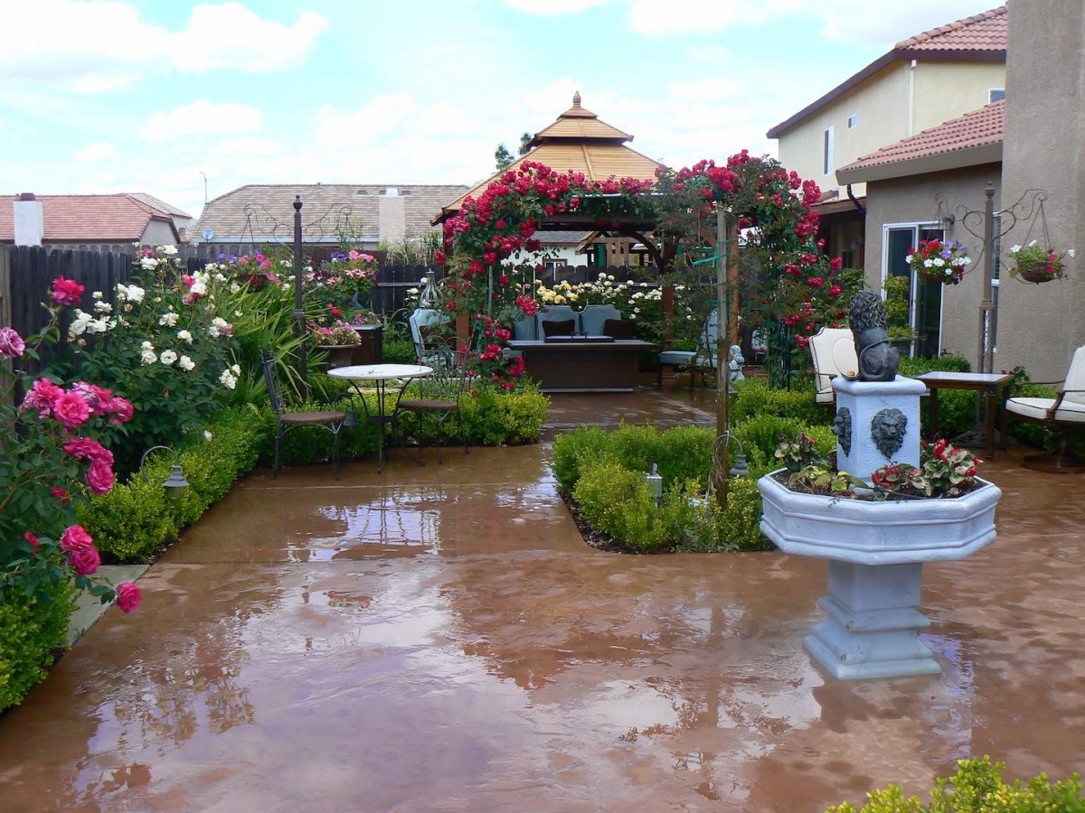 A beautifully landscaped garden featuring a patio, fountain, and vibrant flowers.