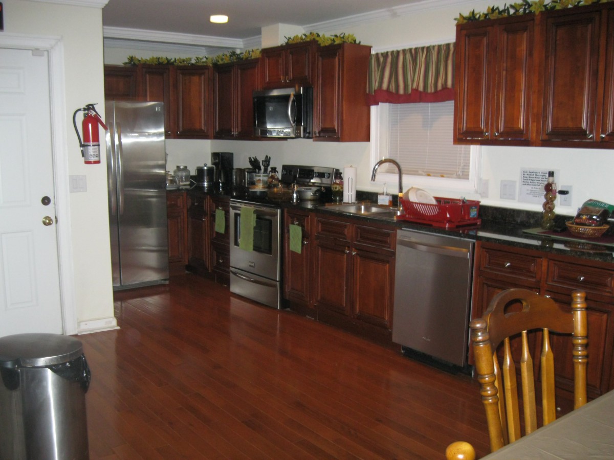 A modern kitchen with wooden cabinets and floors, featuring stainless steel appliances.