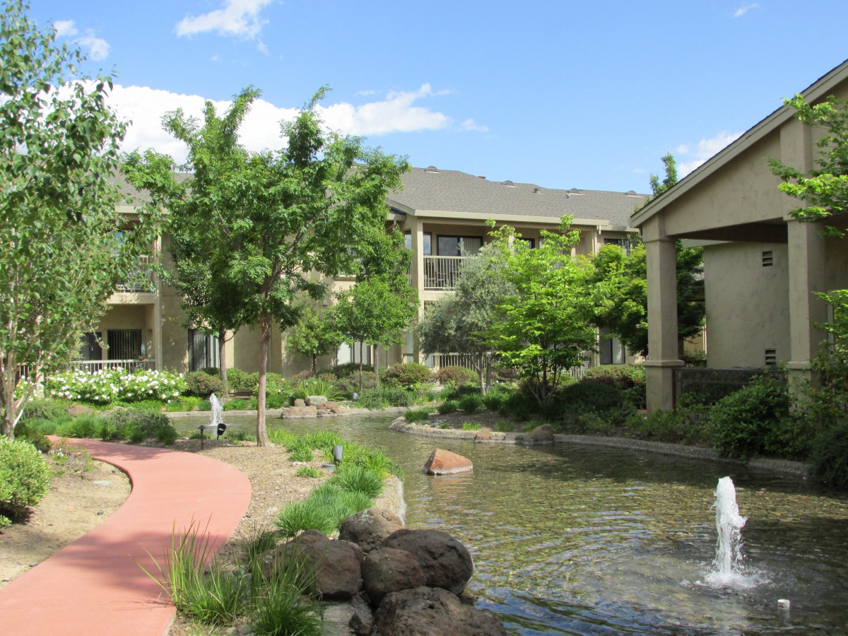 A peaceful courtyard with a fountain, surrounded by lush greenery and an apartment complex.