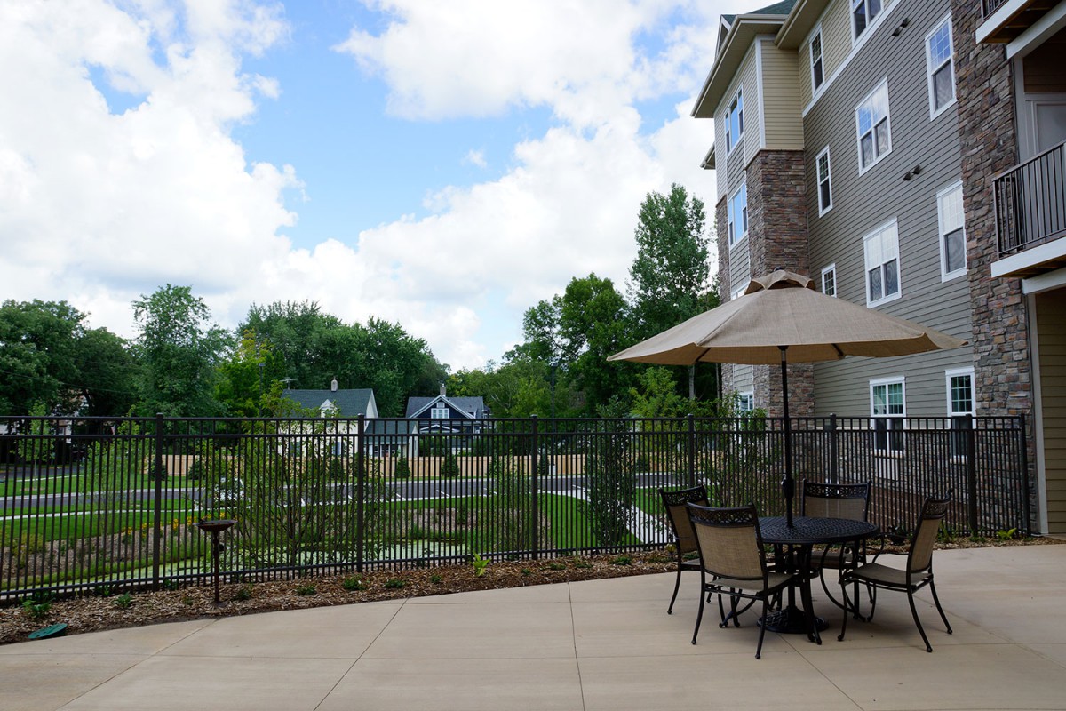 Outdoor patio area with a table, chairs, and umbrella next to an apartment building.