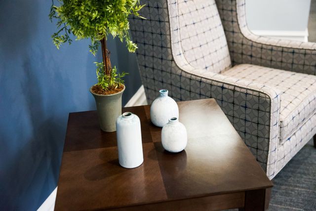 A wooden table with decorative vases and a potted plant next to an upholstered chair.