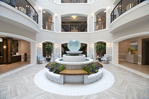 A serene interior atrium featuring a central water fountain surrounded by lush greenery and modern seating arrangements.