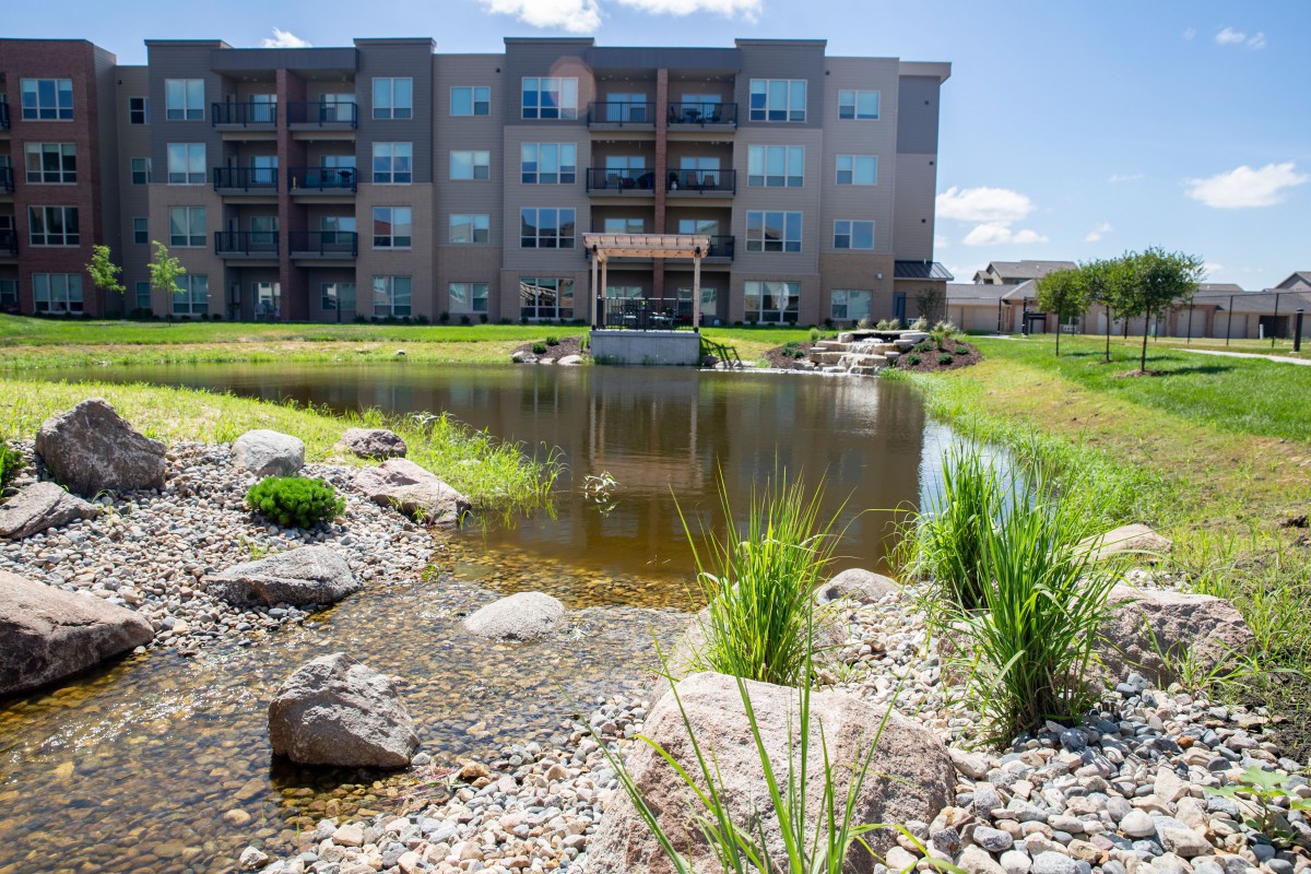 An apartment complex with a landscaped pond surrounded by greenery and rocks.