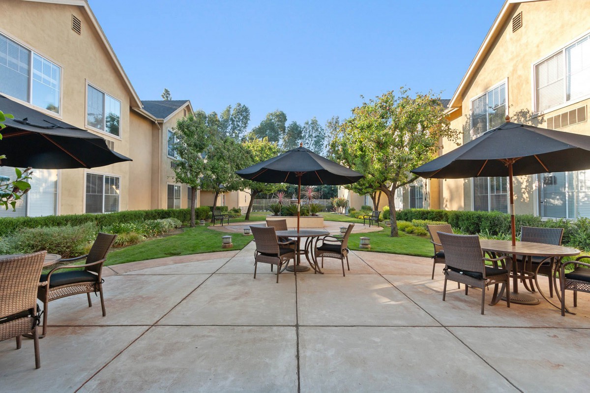 A tranquil apartment courtyard with patio furniture and large umbrellas.