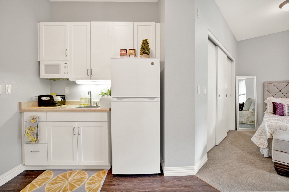 A modern kitchen area in an apartment featuring white cabinets and a refrigerator.