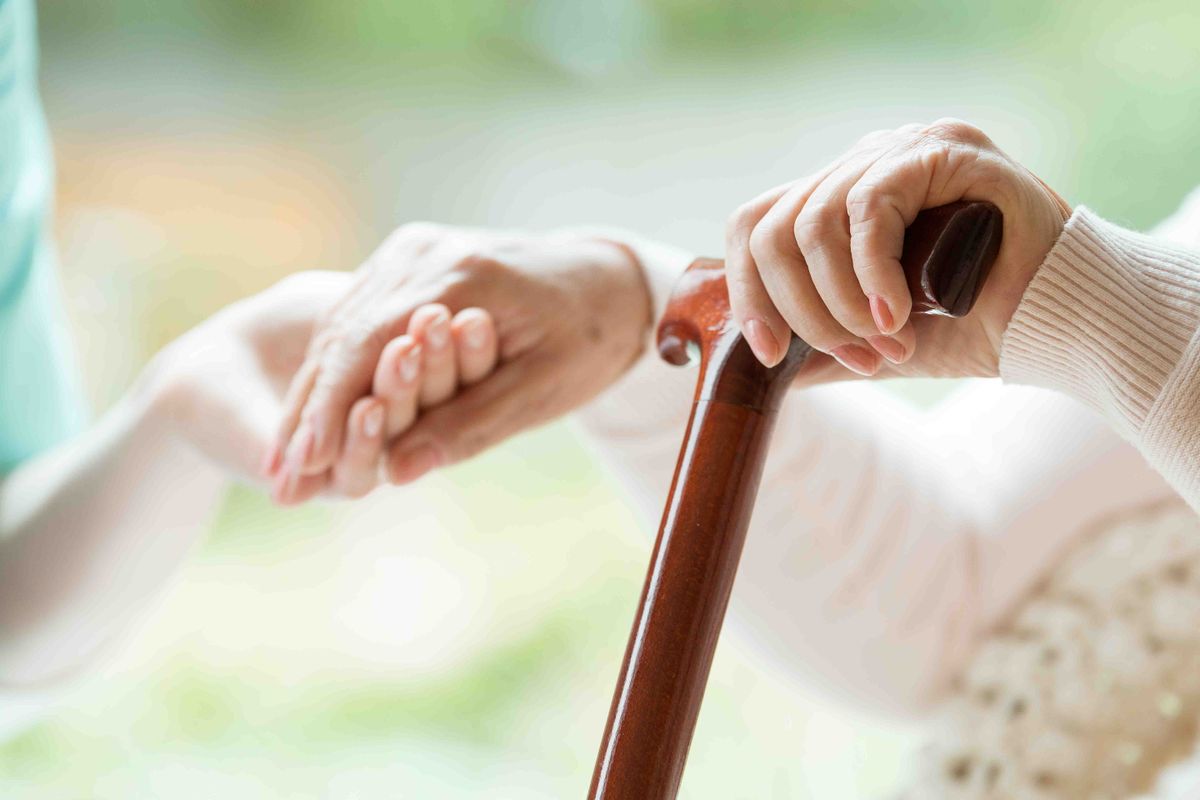 An elderly person holding a cane, demonstrating support and care.