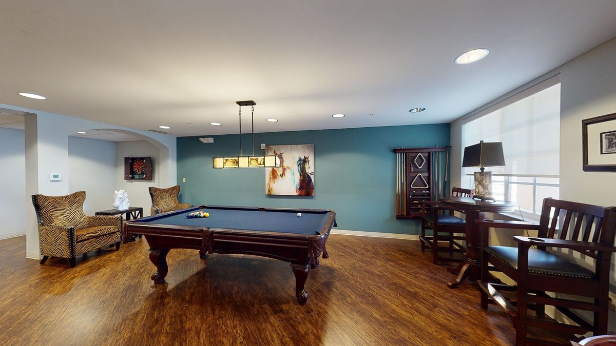 A modern game room featuring a billiards table on wooden flooring, adorned with stylish lighting and decor.