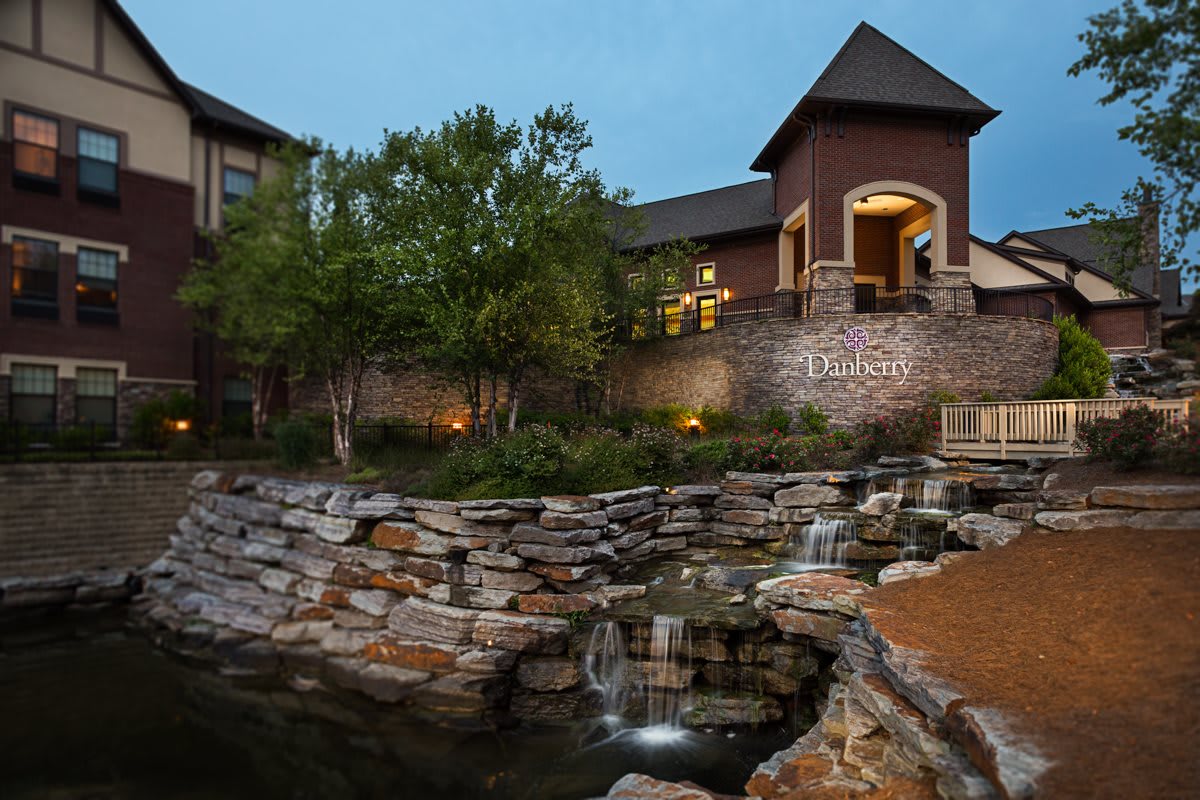A beautiful landscape featuring a building with a stone facade and a cascading water feature surrounded by trees.