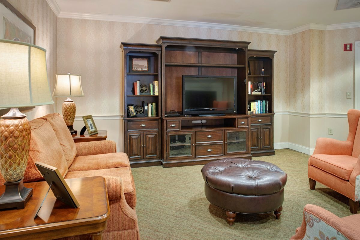 A cozy living room featuring an entertainment center with a television, flanked by shelves and cabinets. A comfortable sofa and round ottoman complete the setting.