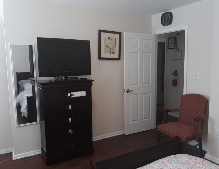 A bedroom with a dresser, television, and a chair near a doorway.