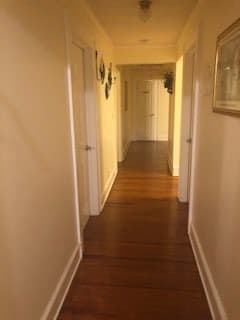 A well-lit hallway with wooden flooring and multiple doors.