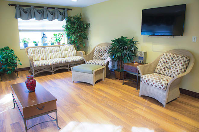 A cozy living room with wicker furniture, a TV on the wall, and decorative plants.
