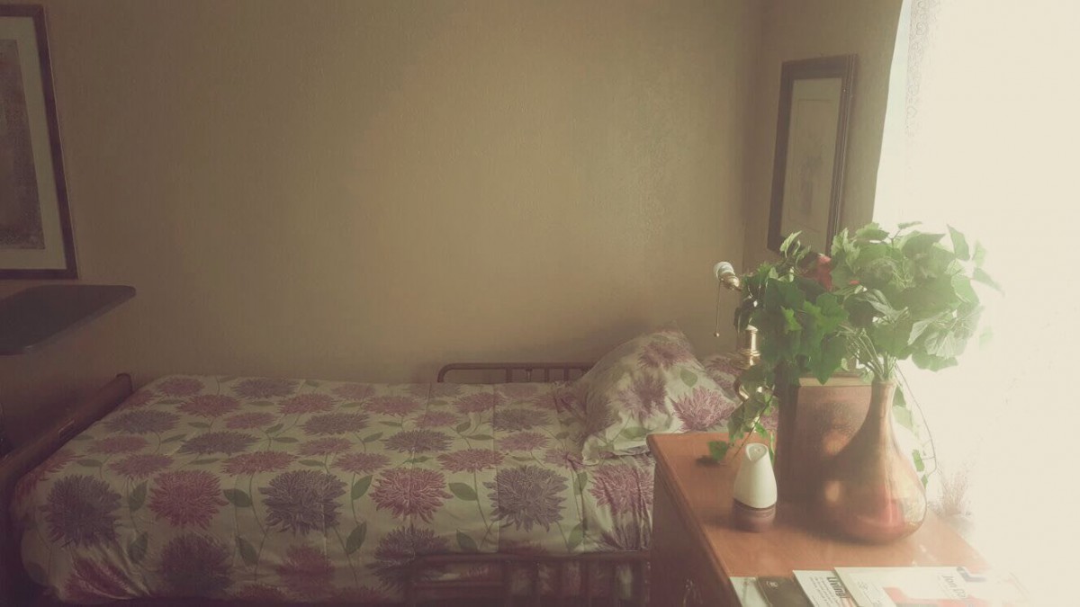 A cozy bedroom with floral bedding and fresh flowers on a dresser.